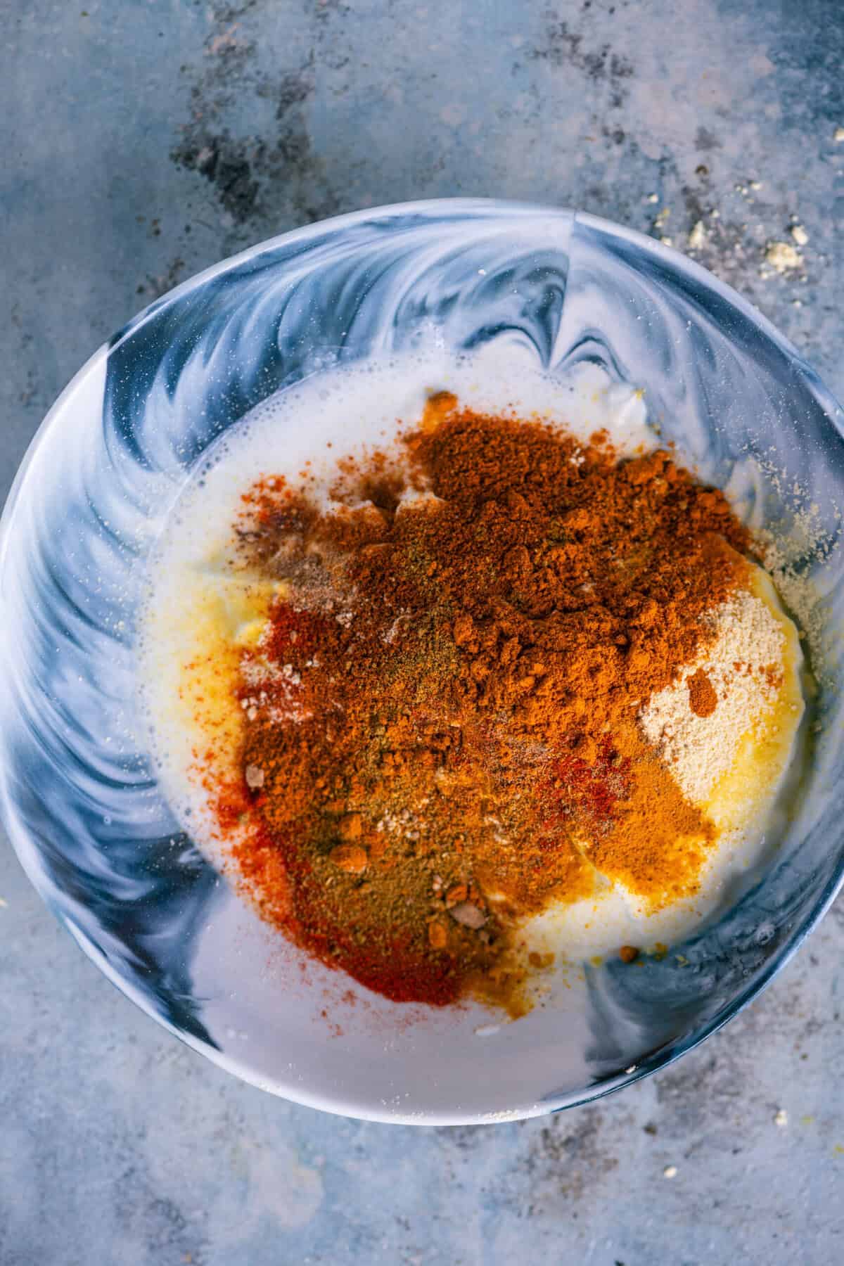 Adding aromatic spice blends: sambhar powder, chole masala, and pav bhaji masala to the yogurt mixture.