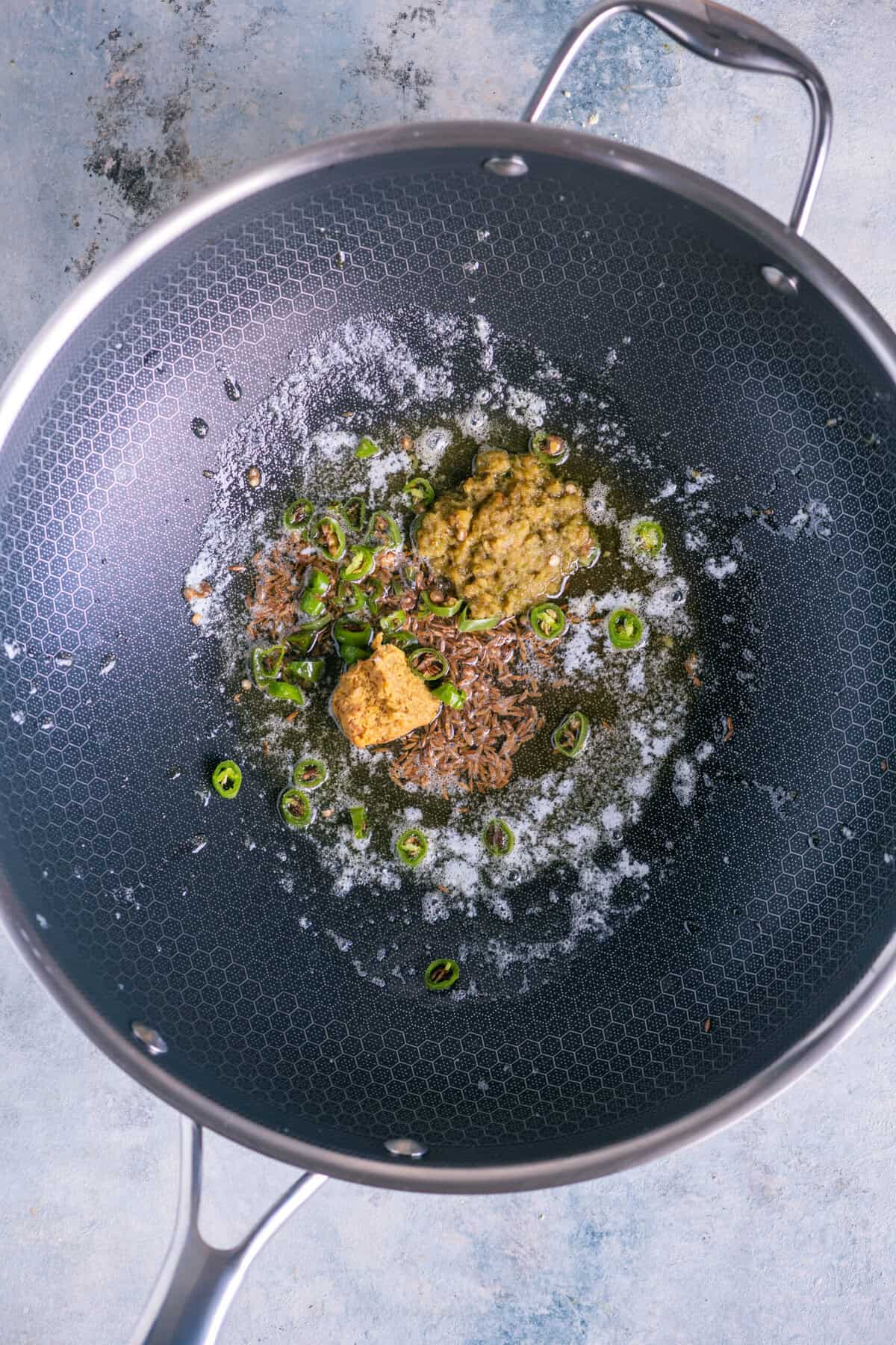 Sautéing ginger paste, garlic paste, and minced green chillies on medium flame to create the flavor base.