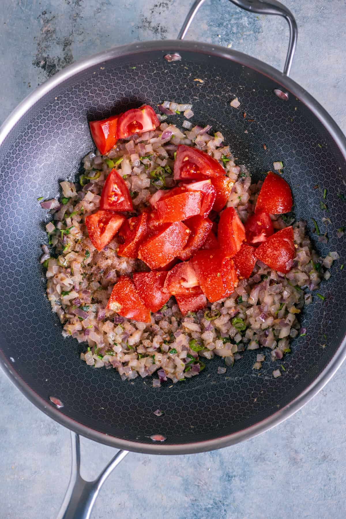 Stirring in chopped tomatoes, salt, and a pinch of sugar; covering and cooking until tomatoes soften.