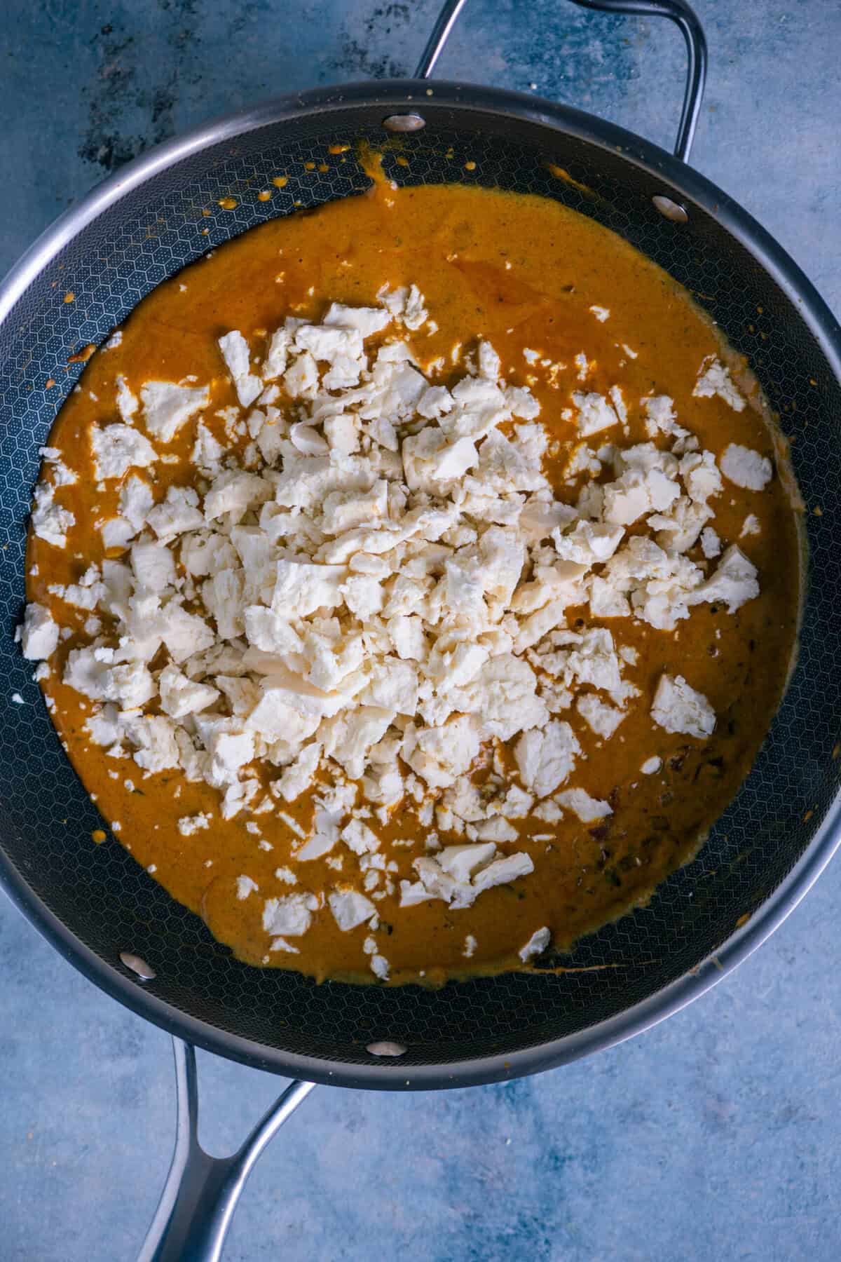 Folding in the crumbled paneer carefully so it absorbs all the flavors without breaking apart.