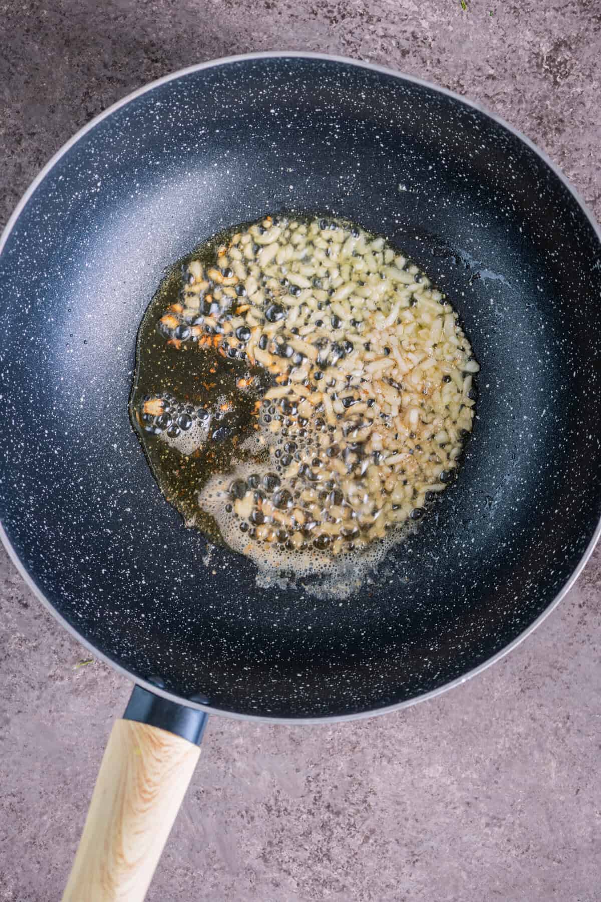 Sautéing garlic in olive oil in a pan for pasta with breadcrumbs.