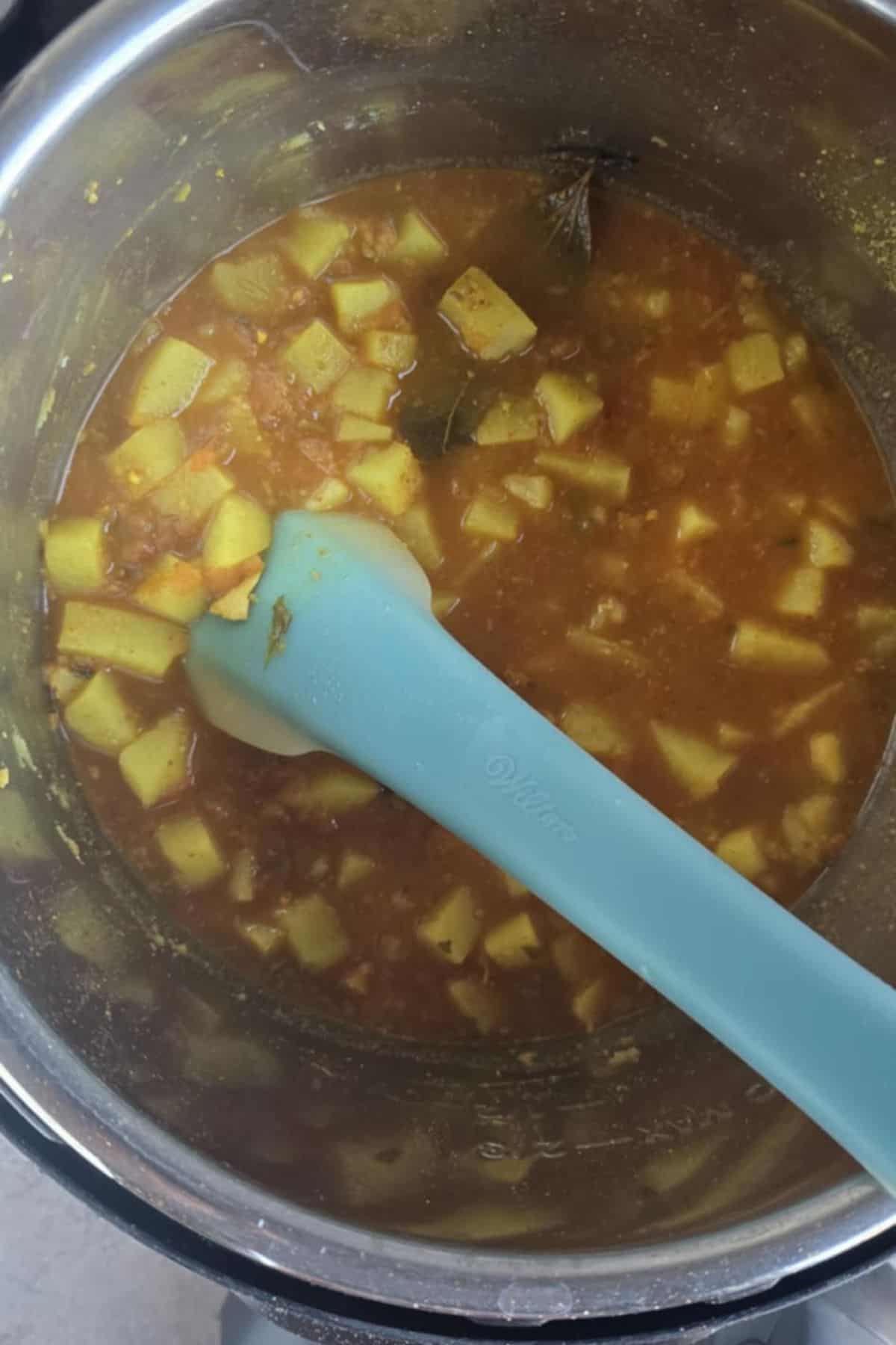 Rasedar aloo being mashed with the back of the ladle to thicken the gravy.