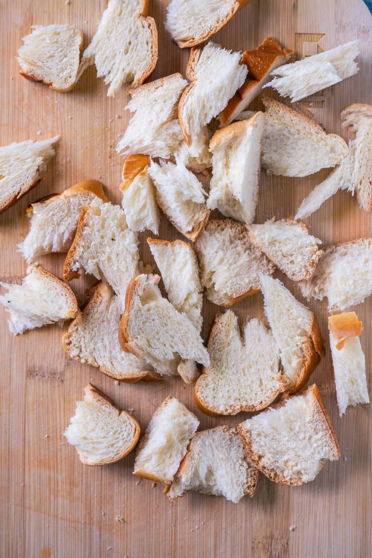 Stale bread slices torn into rustic chunks on a wooden board, ready to be pulsed into breadcrumbs.