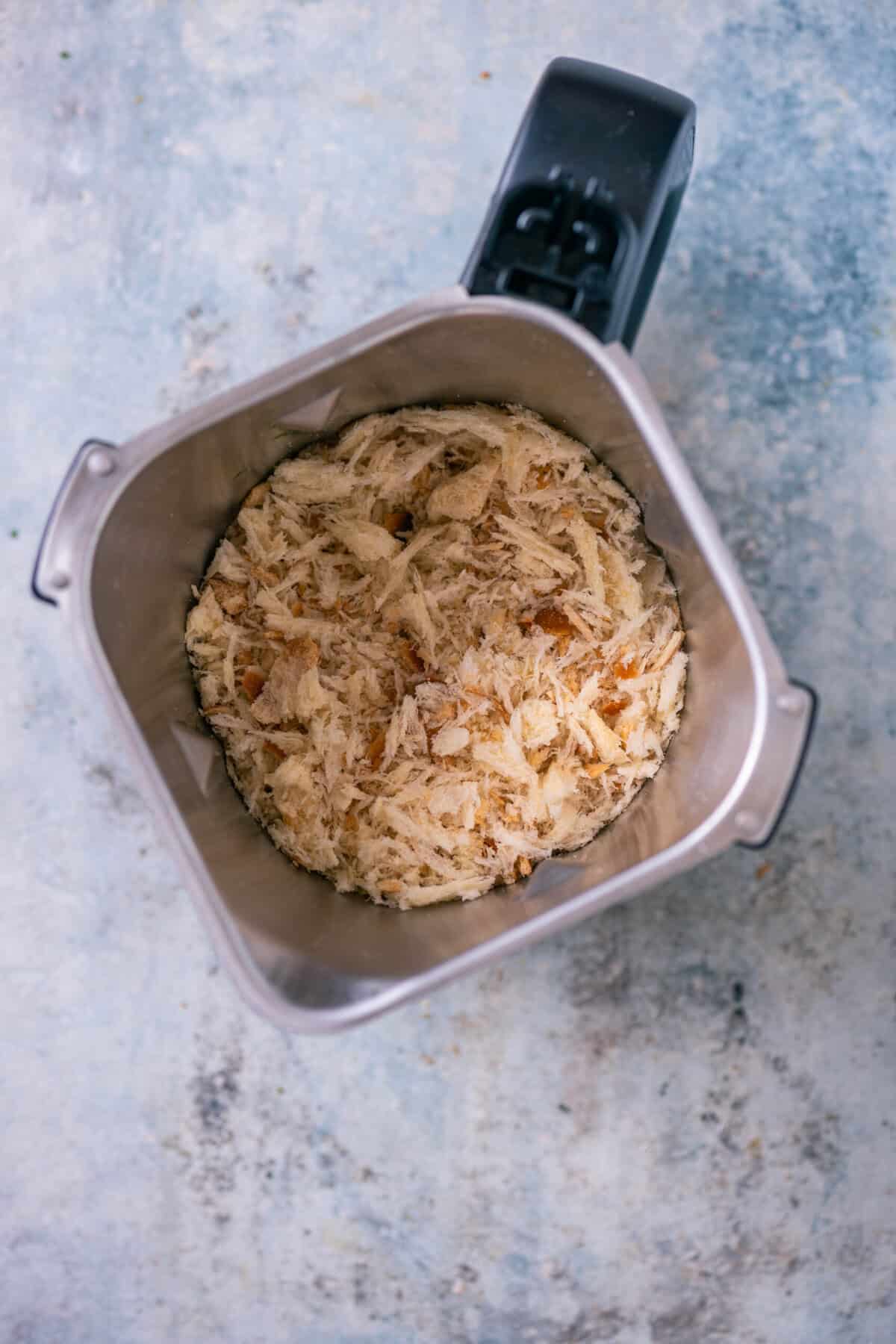 Blender jar filled with torn bread pieces being pulsed into coarse breadcrumbs.