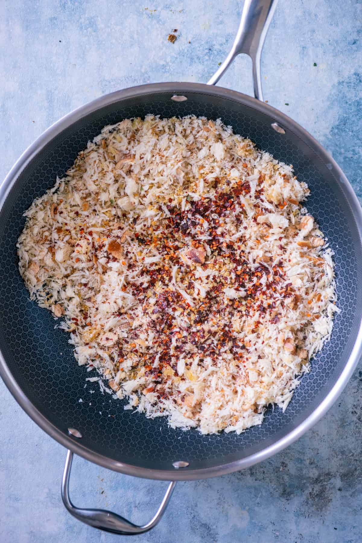 Breadcrumbs in a pan being stirred with garlic flakes, onion powder, and red pepper flakes.