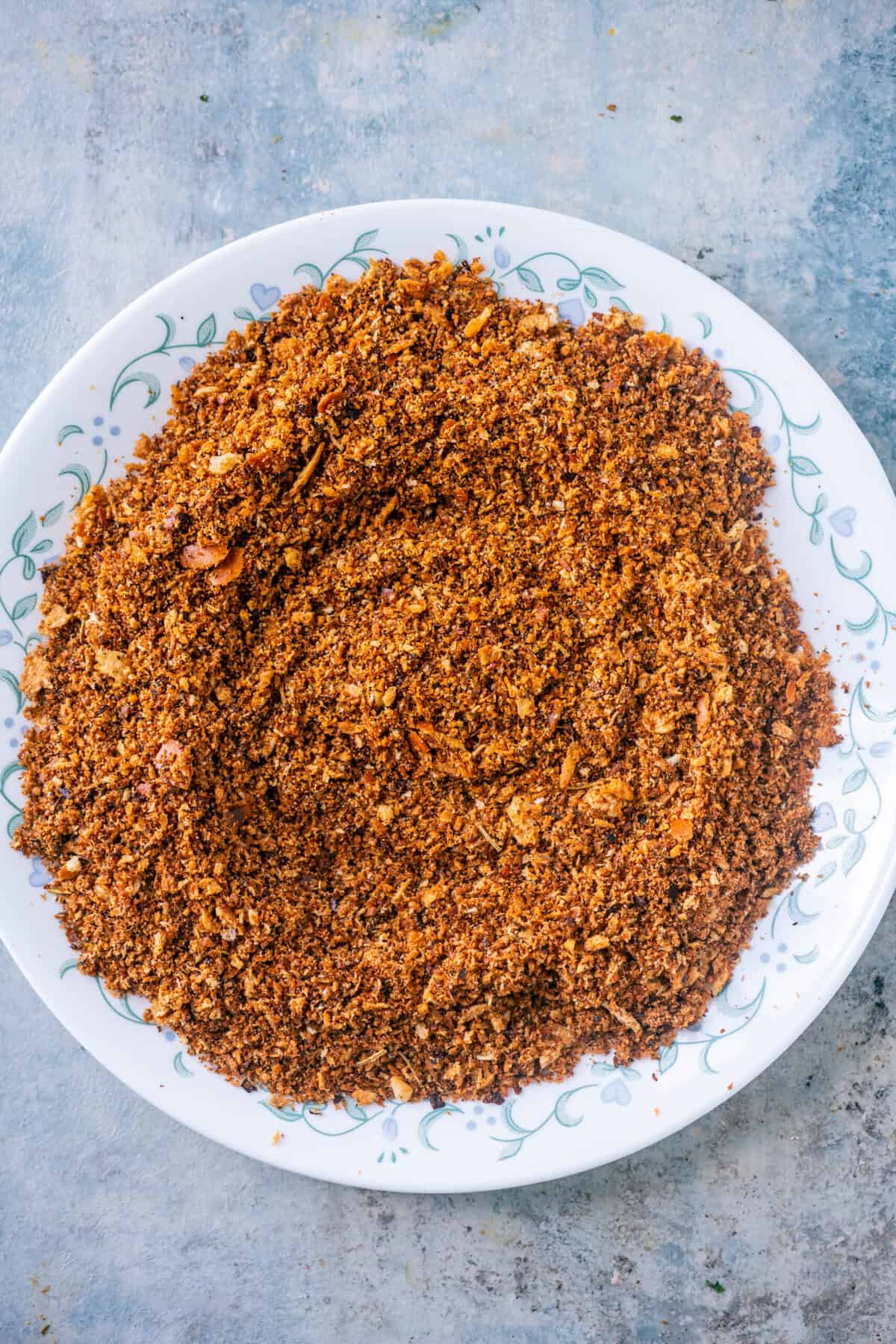 Toasted pangrattato cooling on a plate before being transferred to a glass jar for storage.