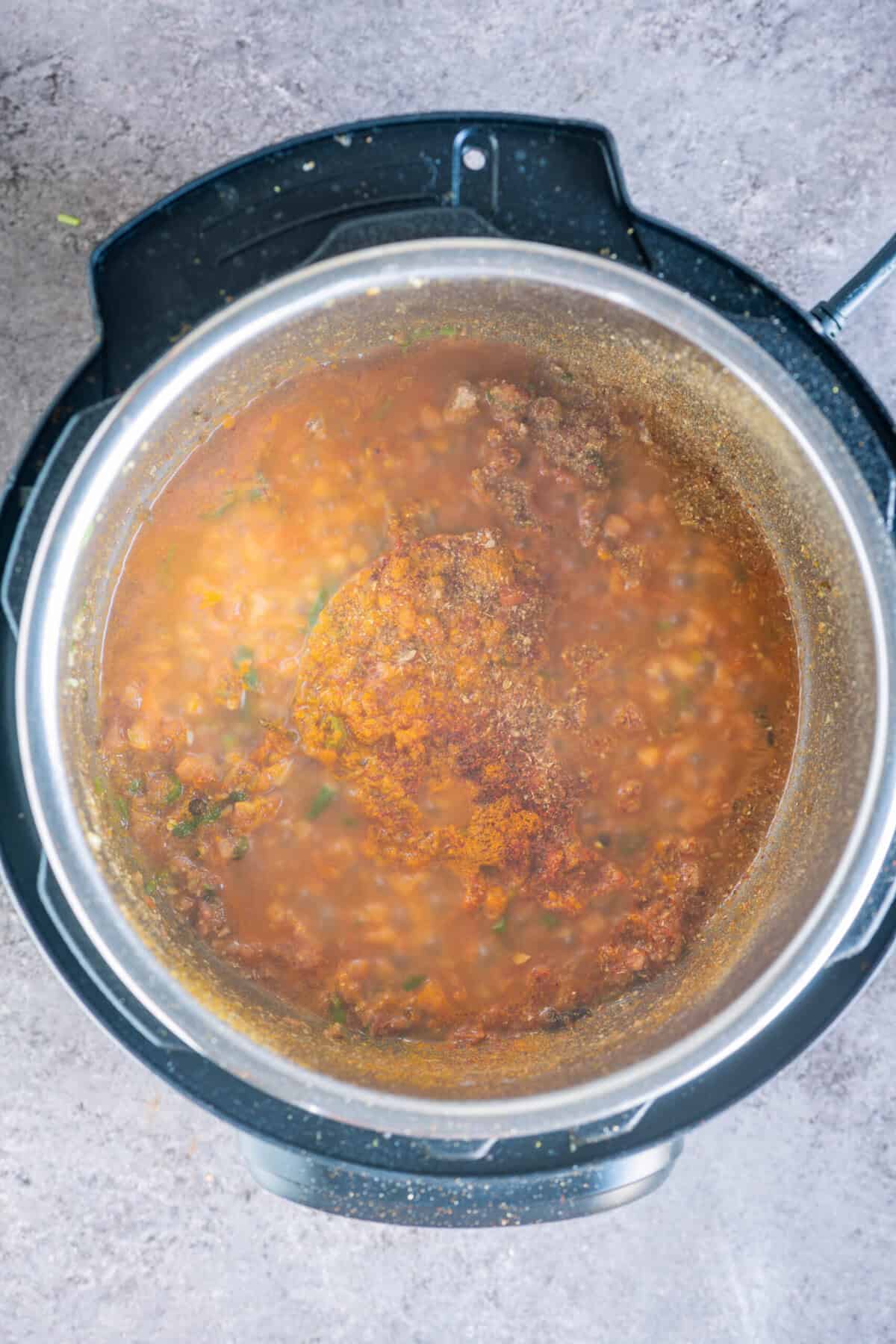 Turmeric, coriander, red chili powder, and amchur being mixed with tomatoes in the Instant Pot to bloom the spices for rasedar aloo.