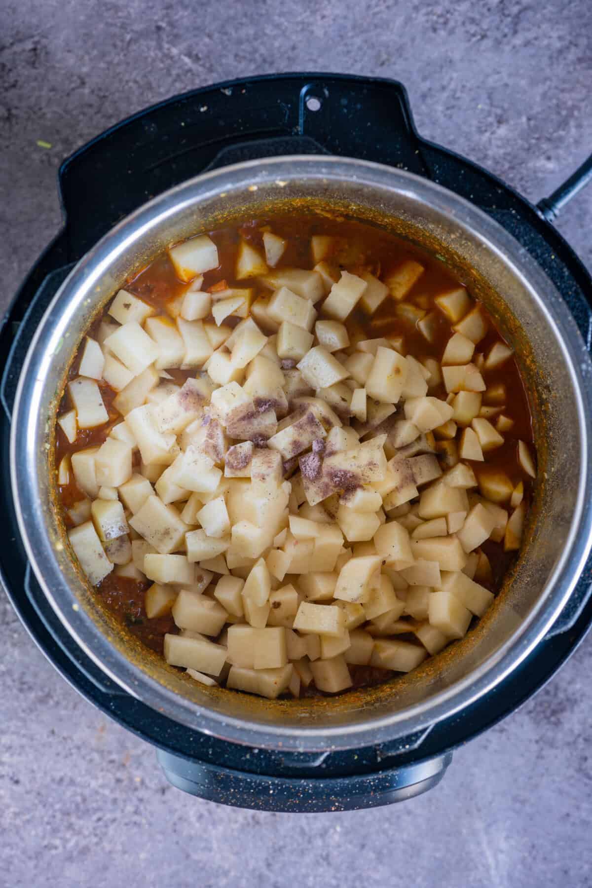 Potato cubes coated in spiced tomato masala with black salt added, preparing the potato curry for pressure cooking.