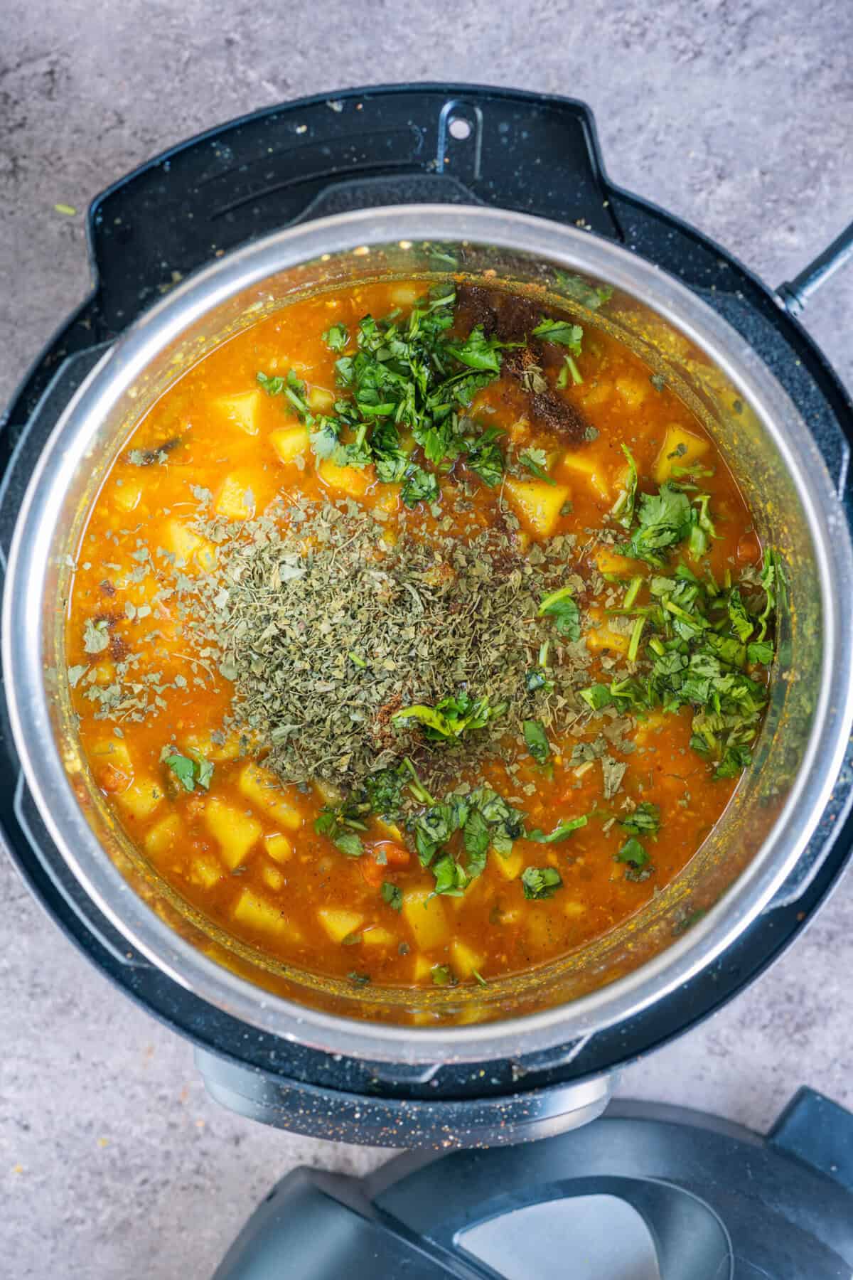 Cooked potatoes being lightly mashed in the pot to thicken the gravy and achieve the classic rasedar aloo texture.