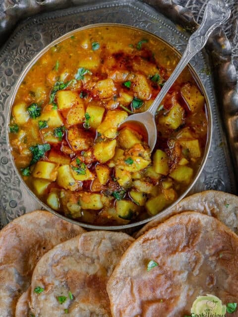 Close-up of creamy rasedar aloo curry with golden puffed puris on the side, showcasing the saucy texture and homemade spice blend.
