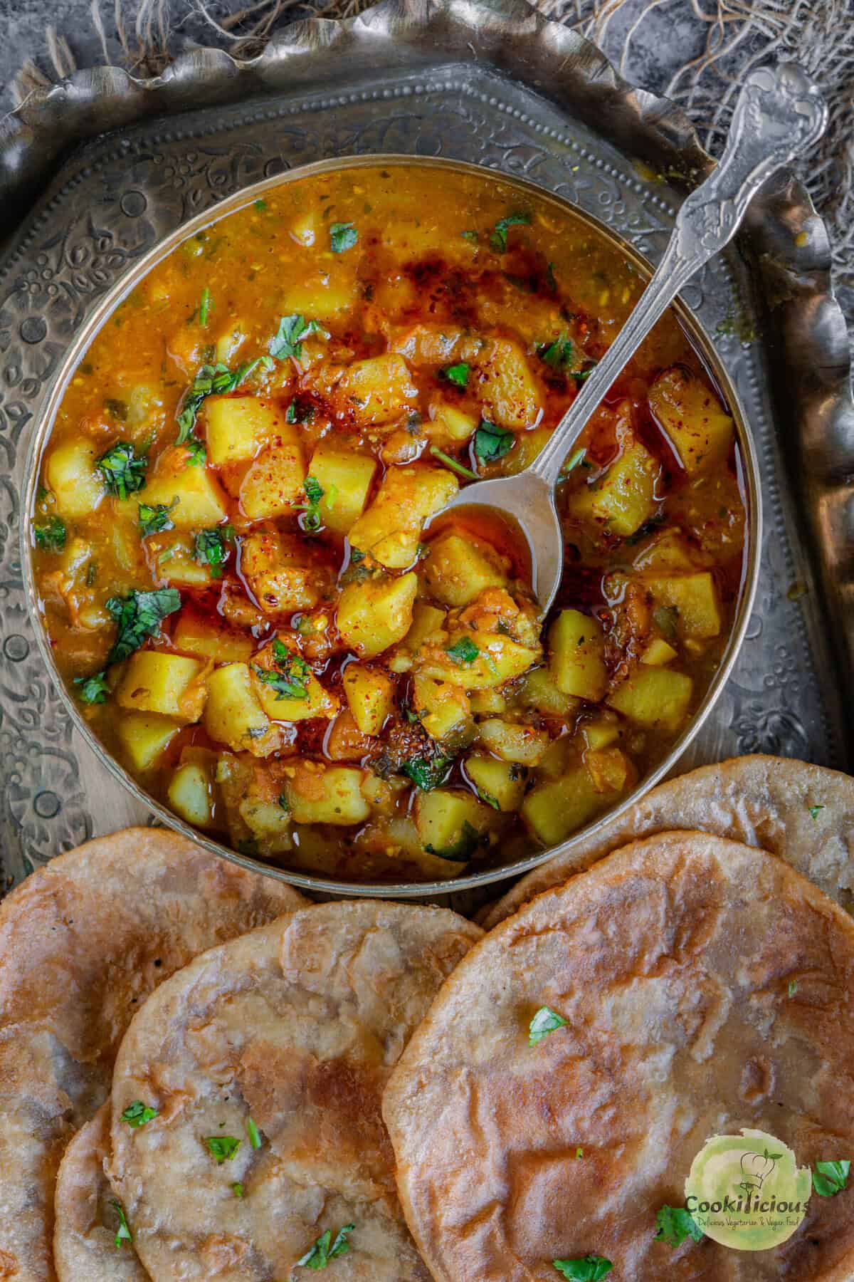 creamy rasedar aloo curry with golden puffed puris on the side, showcasing the saucy texture and homemade spice blend.