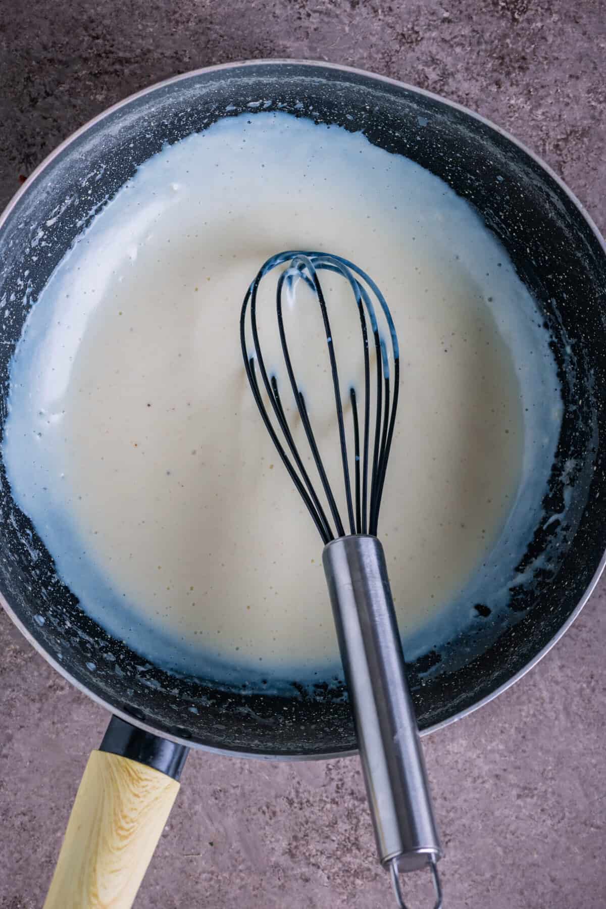 Alfredo sauce mix being whisked into the warm milk-butter mixture.