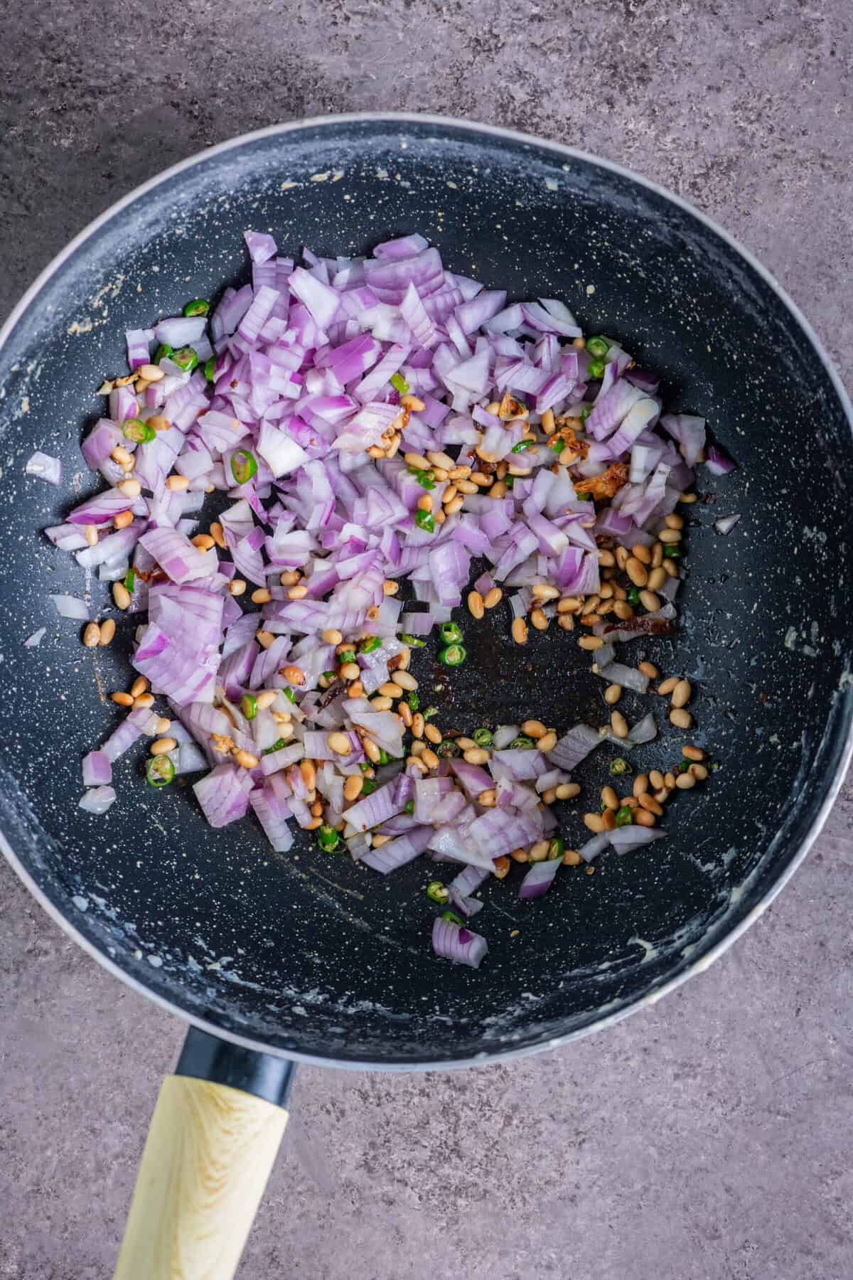 Chopped onions and green chilies sautéing with toasted pine nuts.