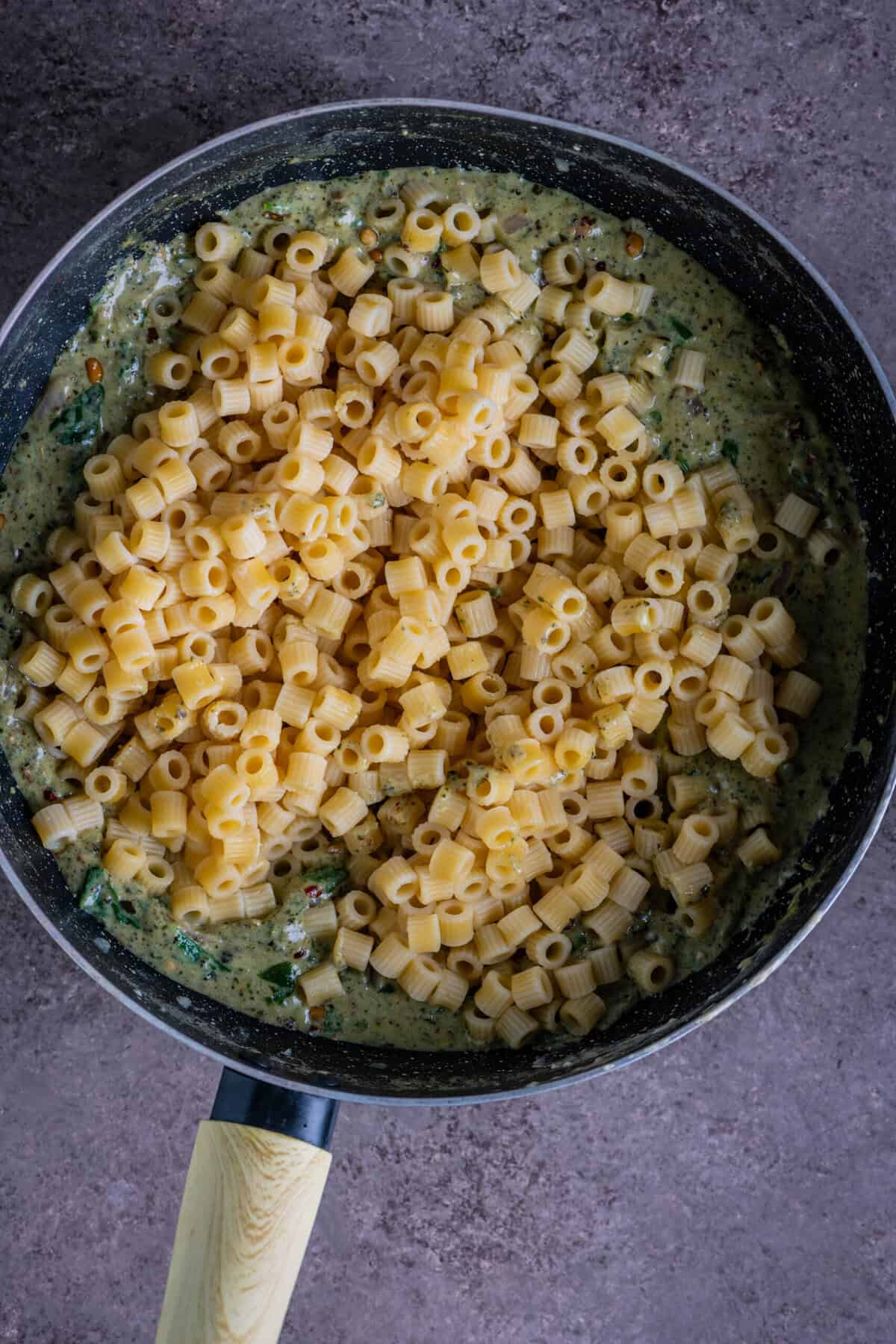 Cooked pasta being folded into the creamy pesto sauce.