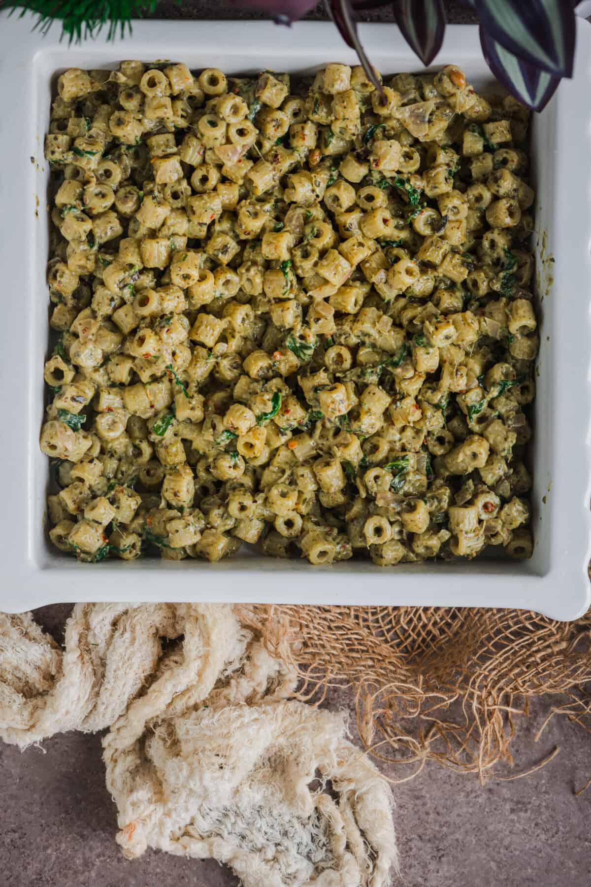 Creamy pesto pasta spread evenly in a buttered baking dish.