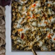 Baked pesto pasta topped with burrata and herbs in a ceramic casserole pan.