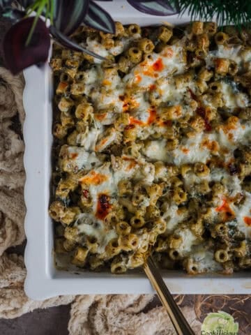 Baked pesto pasta topped with burrata and herbs in a ceramic casserole pan.
