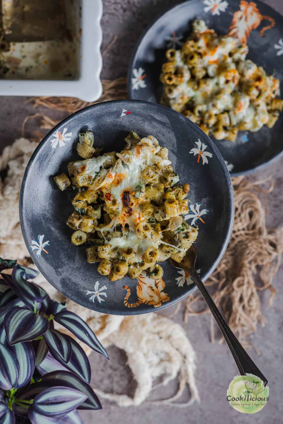 Serving of creamy pesto pasta bake on a plate with melted cheese strands.
