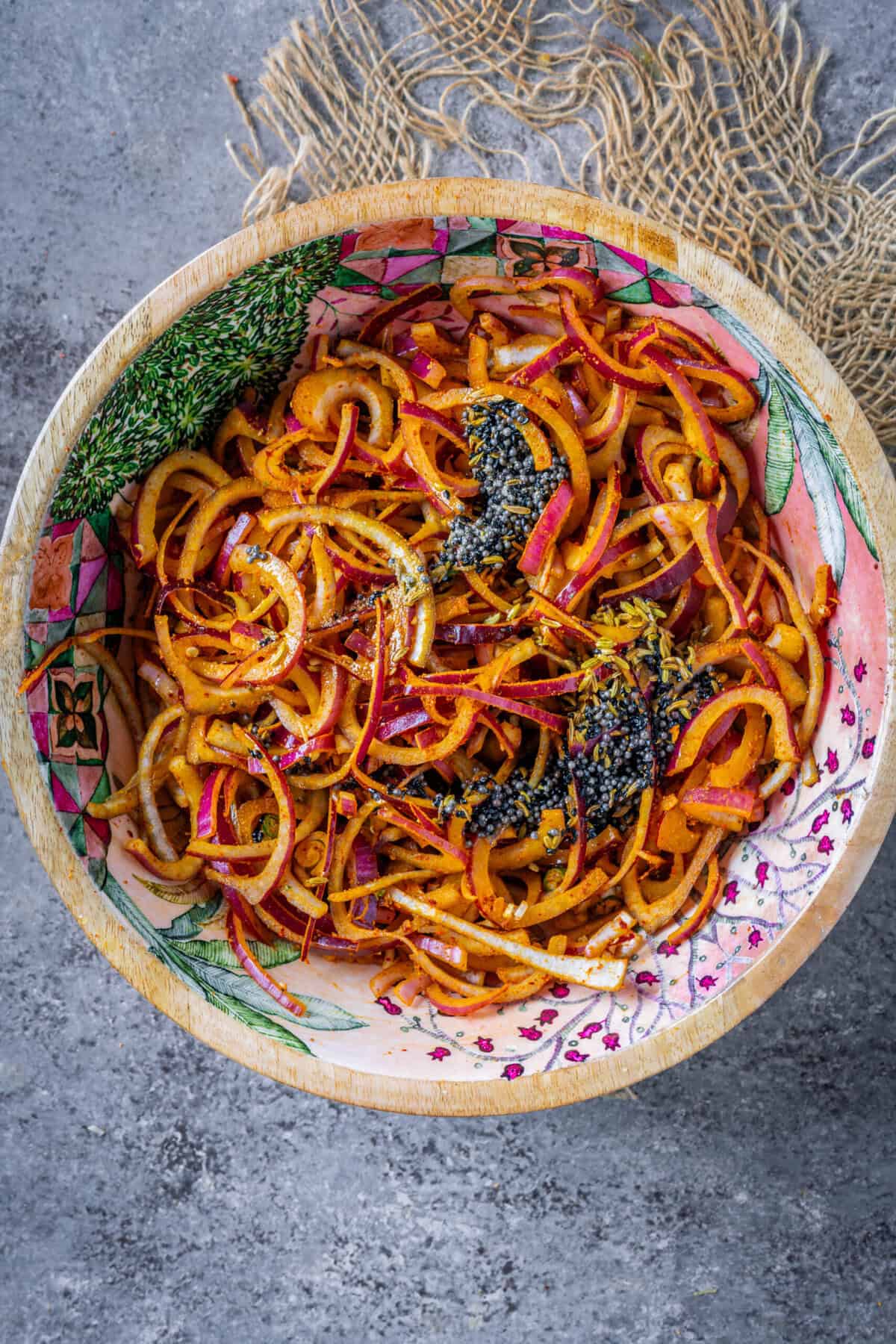 Hot tadka of mustard seeds, asafoetida, fennel seeds, and kalonji poured over the red onion salad.