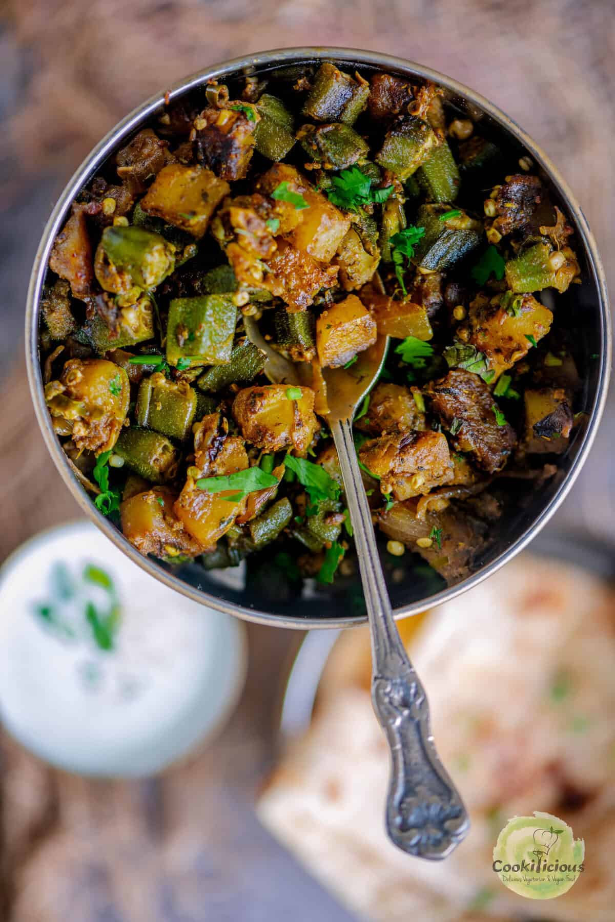 Restaurant-style Aloo Bhindi served in a skillet with tender potatoes and crispy okra, garnished with cilantro and lemon juice.