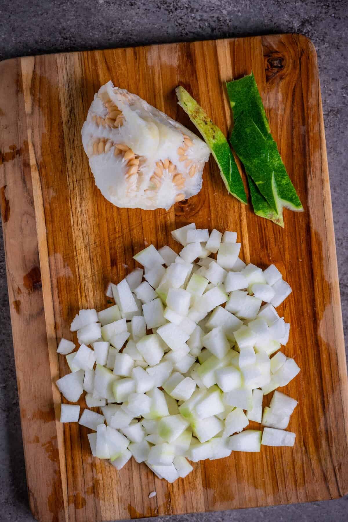 Chopped white pumpkin cubes on a cutting board after removing seeds and peeling for Poosanikai Kootu.