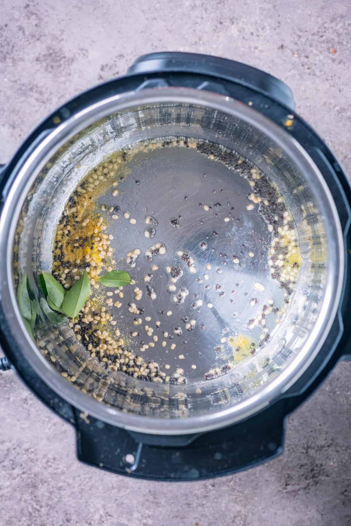 Mustard seeds, urad dal, and curry leaves sizzling in vegan ghee in an Instant Pot for Poosanikai Kootu.