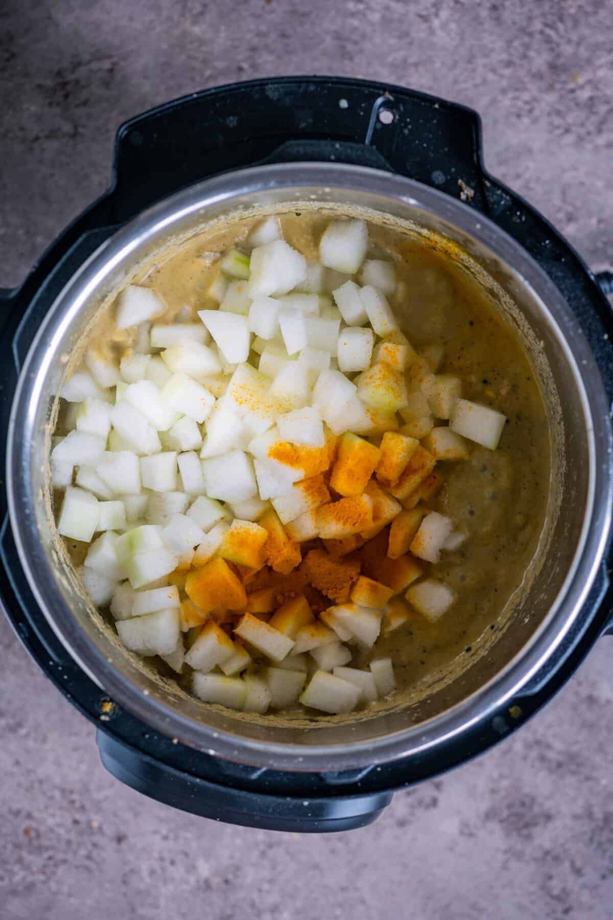 Cubes of white pumpkin (vellai poosanikai) added to the Instant Pot with turmeric powder.