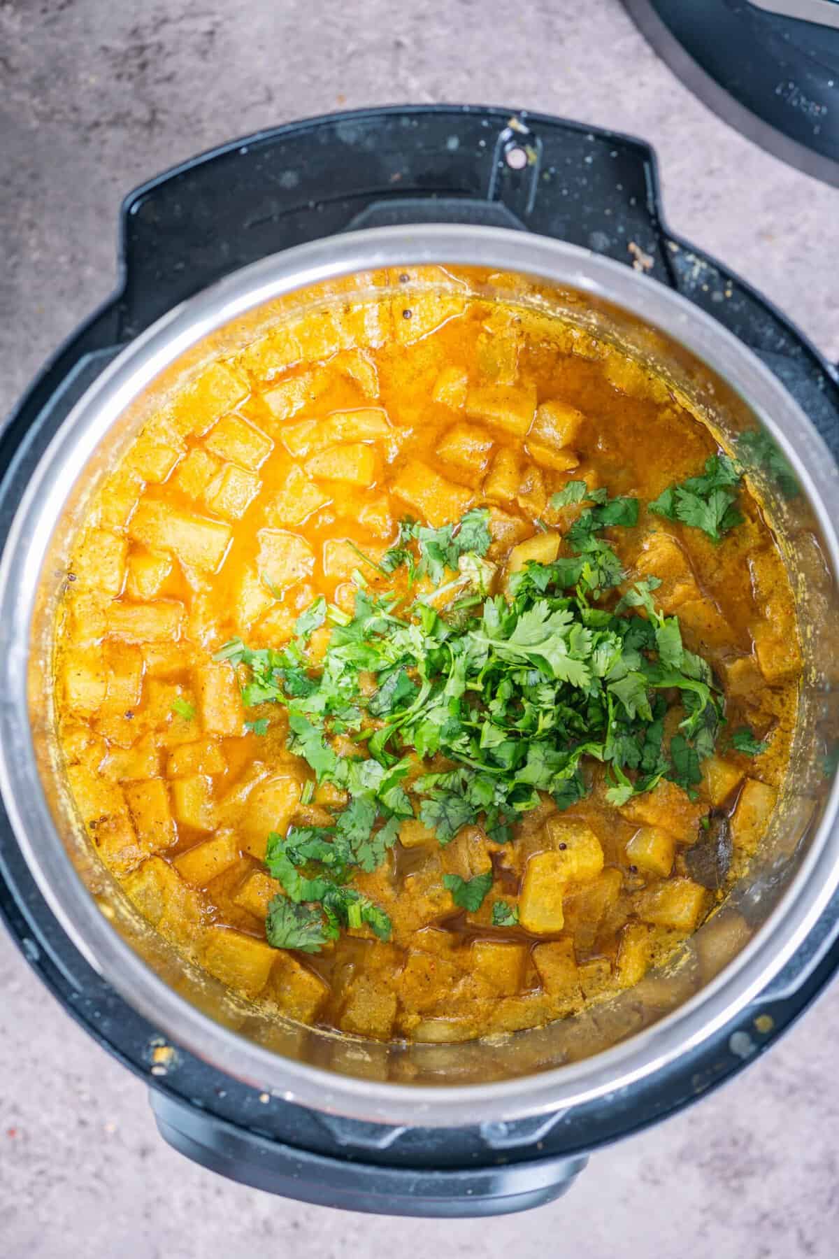 Cooked Poosanikai Kootu being garnished with fresh cilantro after pressure cooking.
