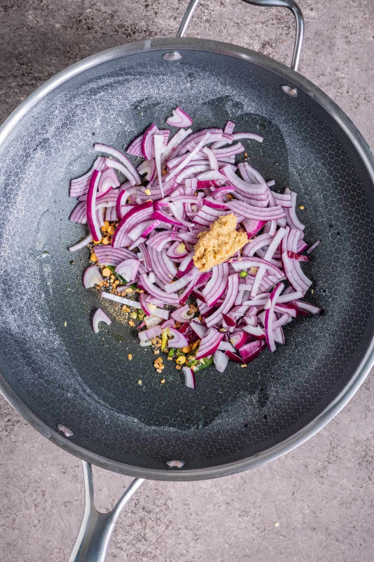 Onions and ginger sauteing in pan while preparing tomato vegetable upma.