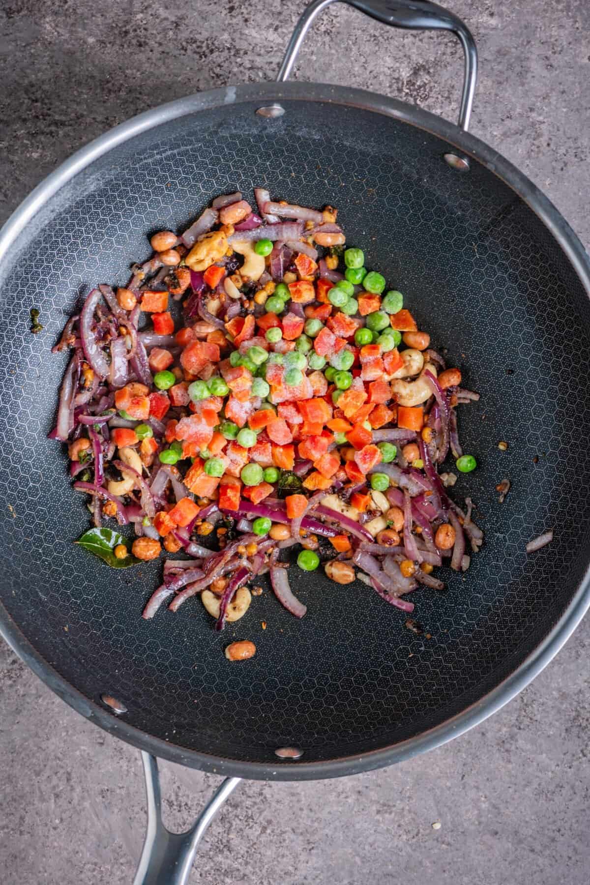 Mixed vegetables including peas and carrots cooking in pan for rava upma recipe.