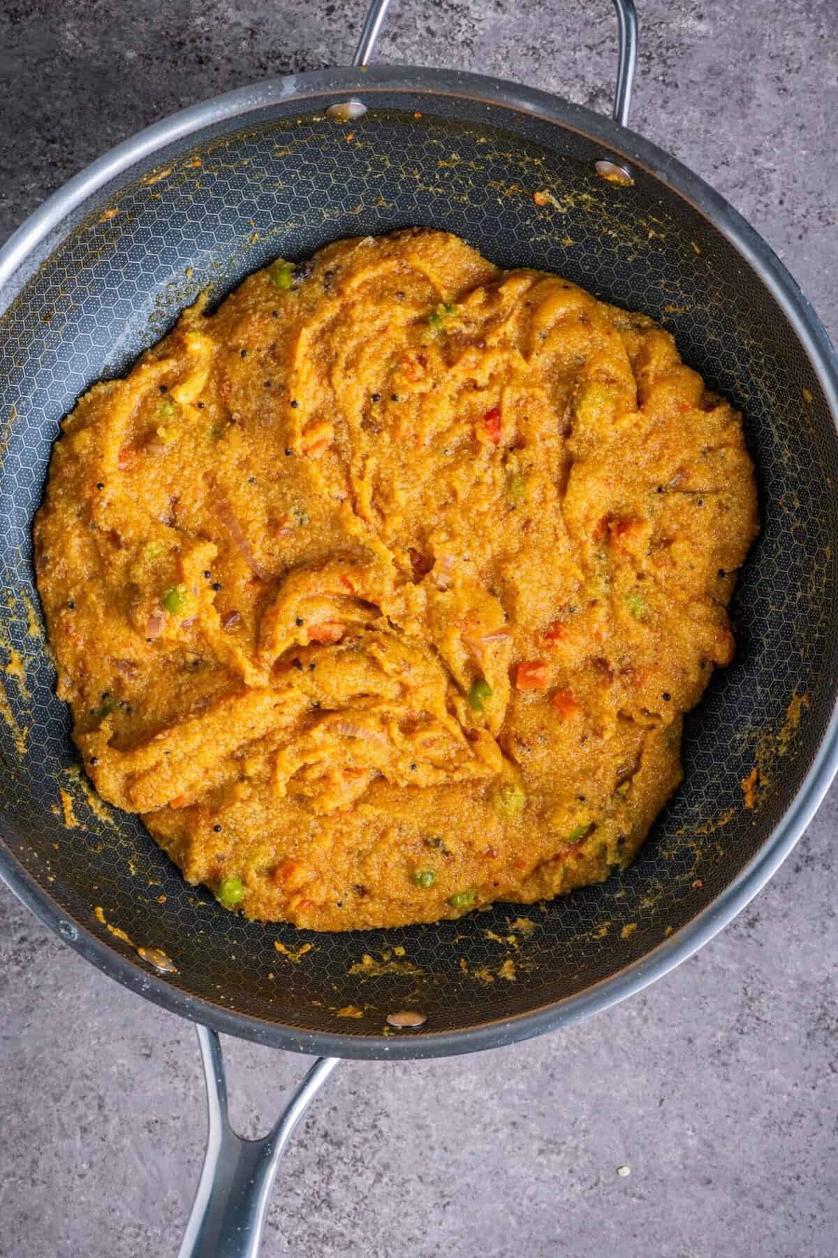 Tomato rava upma thickening and cooking in pan until fluffy texture forms.