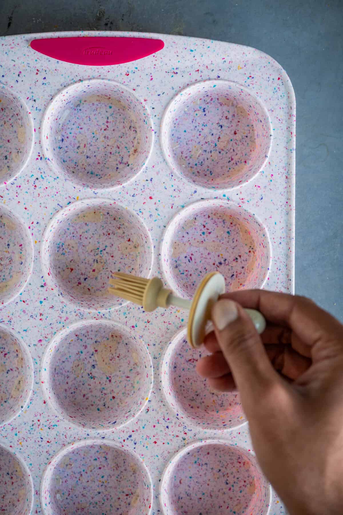 Greasing a muffin tray with oil before adding cupcake batter.