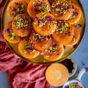 Gulab Jamun Cupcakes topped with pistachios and rose petals served in a plate.