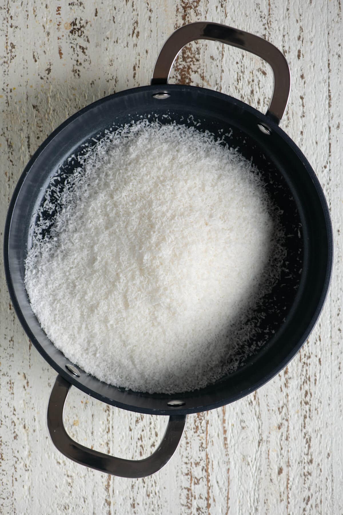 Desiccated coconut being dry roasted in a pan until golden.