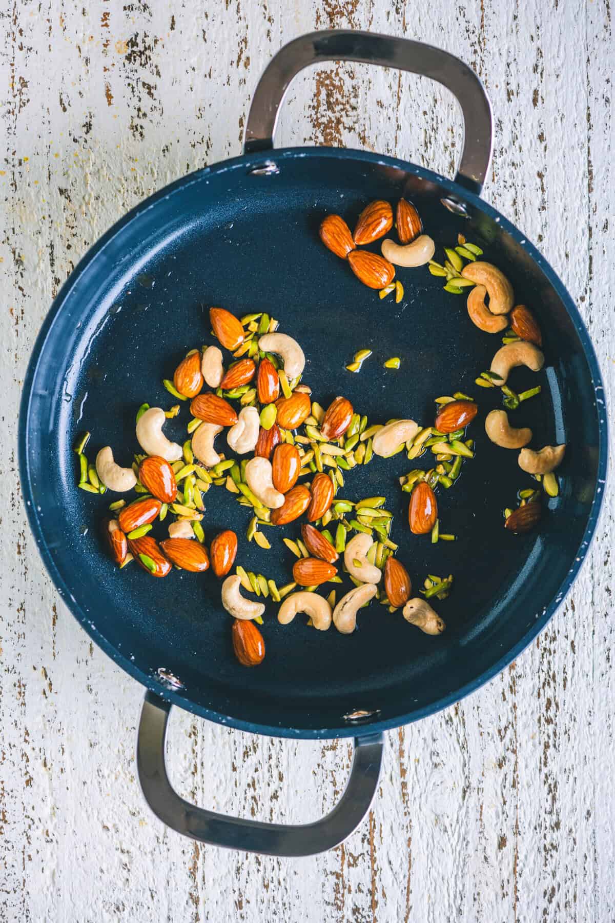 Cashews, almonds, and pistachios frying in ghee in a pan.