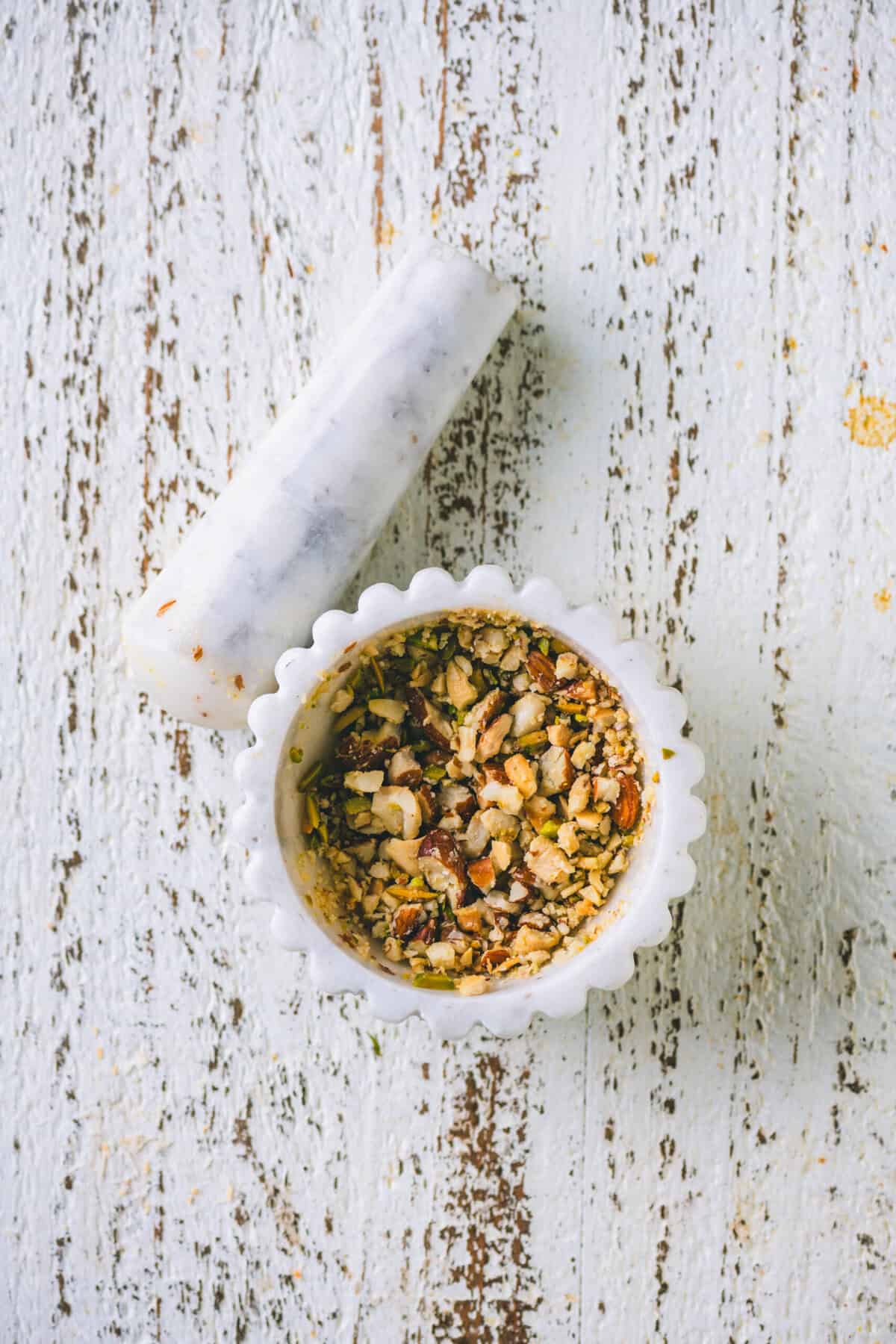 Coarsely crushed mixed nuts in a mortar and pestle for coconut barfi topping.