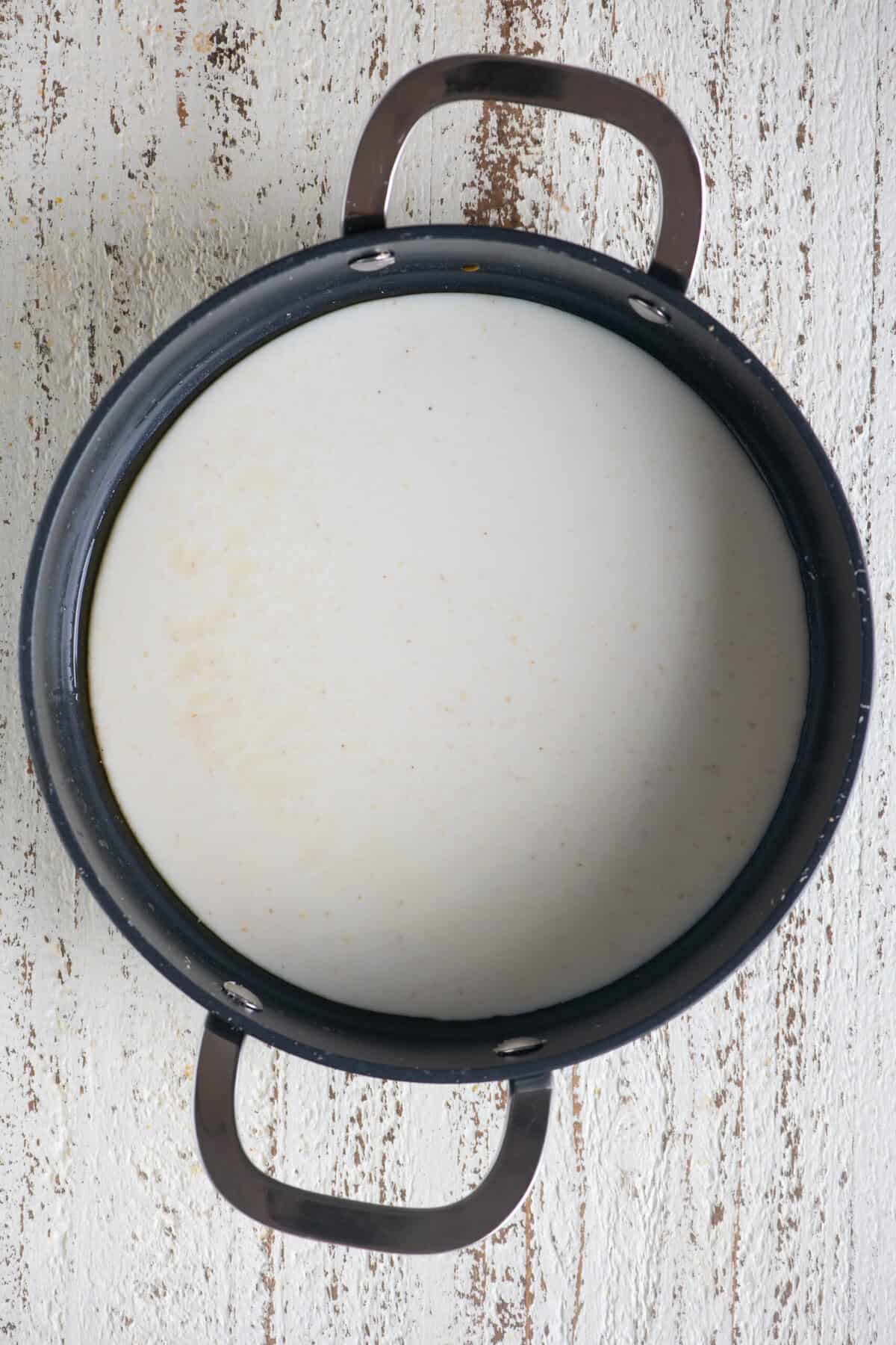 Sautéing soaked rava and milk mixture with ghee in a pan.