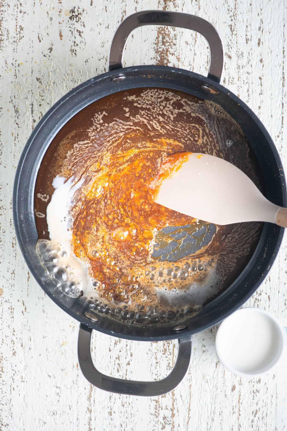 Milk being poured into the caramel mixture gradually.