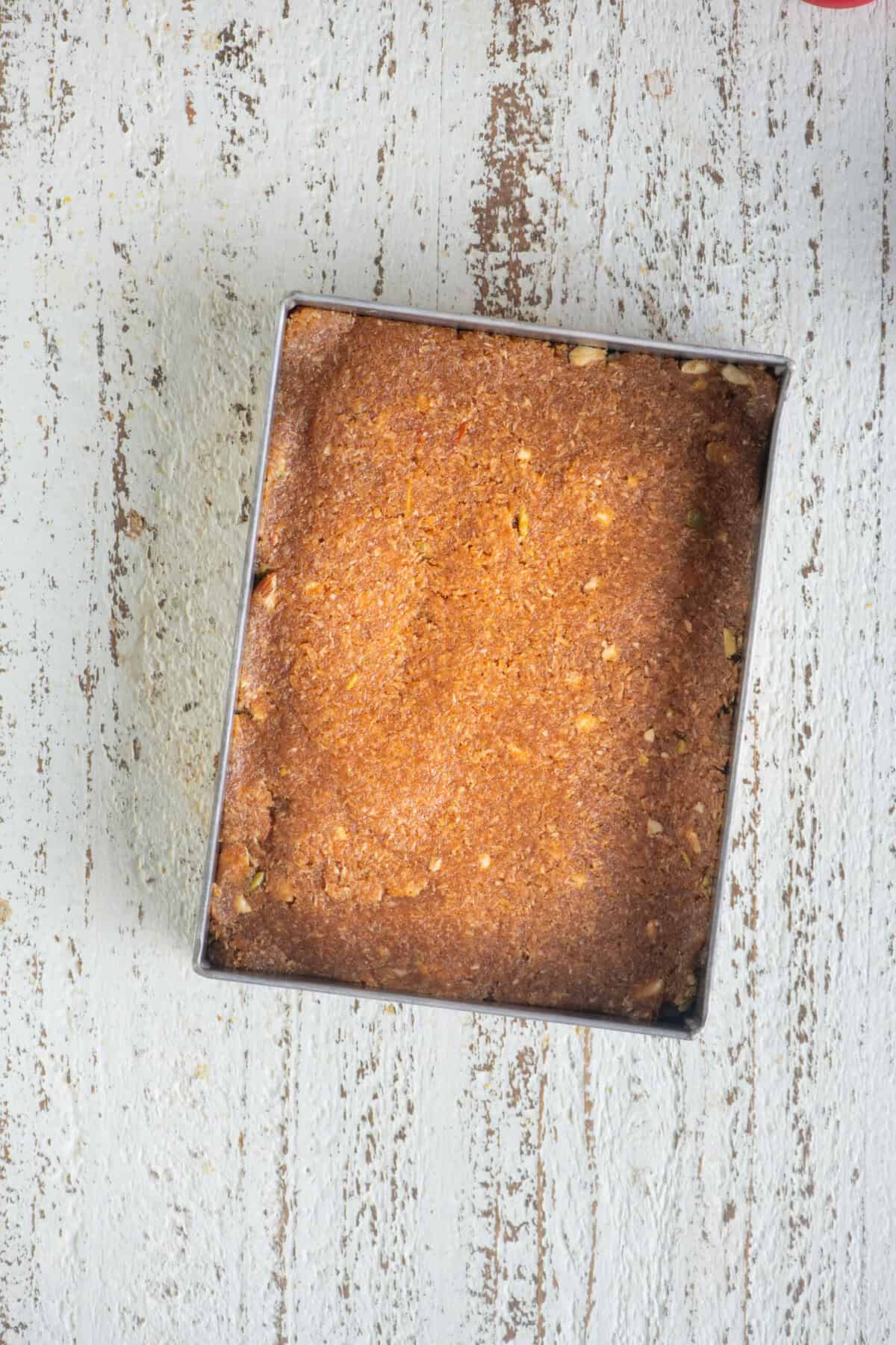 Caramel coconut barfi mixture spread evenly in a greased tray.