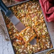 Caramel coconut barfi (nariyal barfi) being sliced into squares in the pan with a metal spatula.