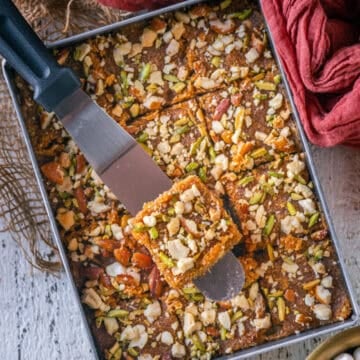 Caramel coconut barfi (nariyal barfi) being sliced into squares in the pan with a metal spatula.