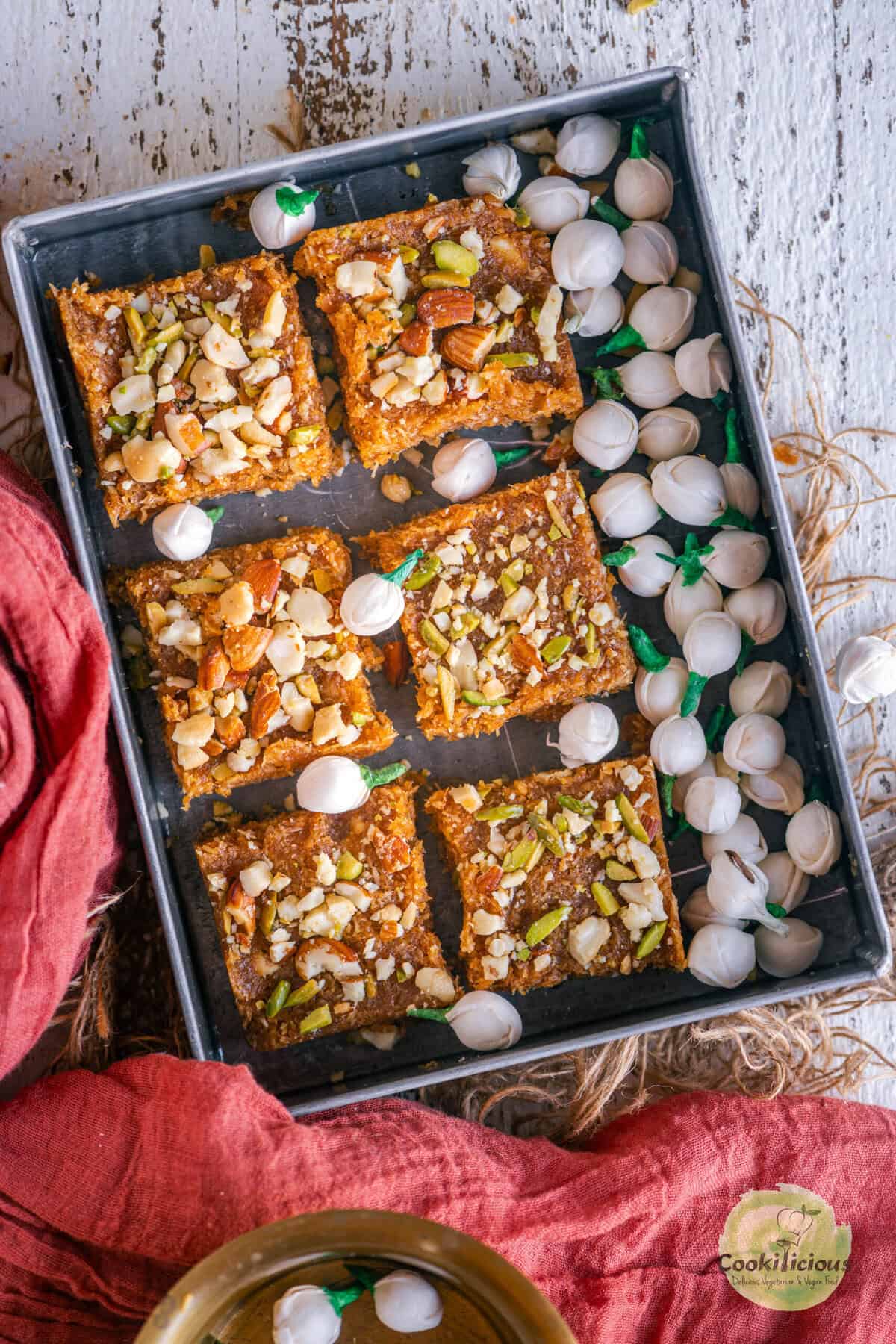 Caramel coconut barfi squares topped with almonds, pistachios, and cashews on a rustic metal tray.