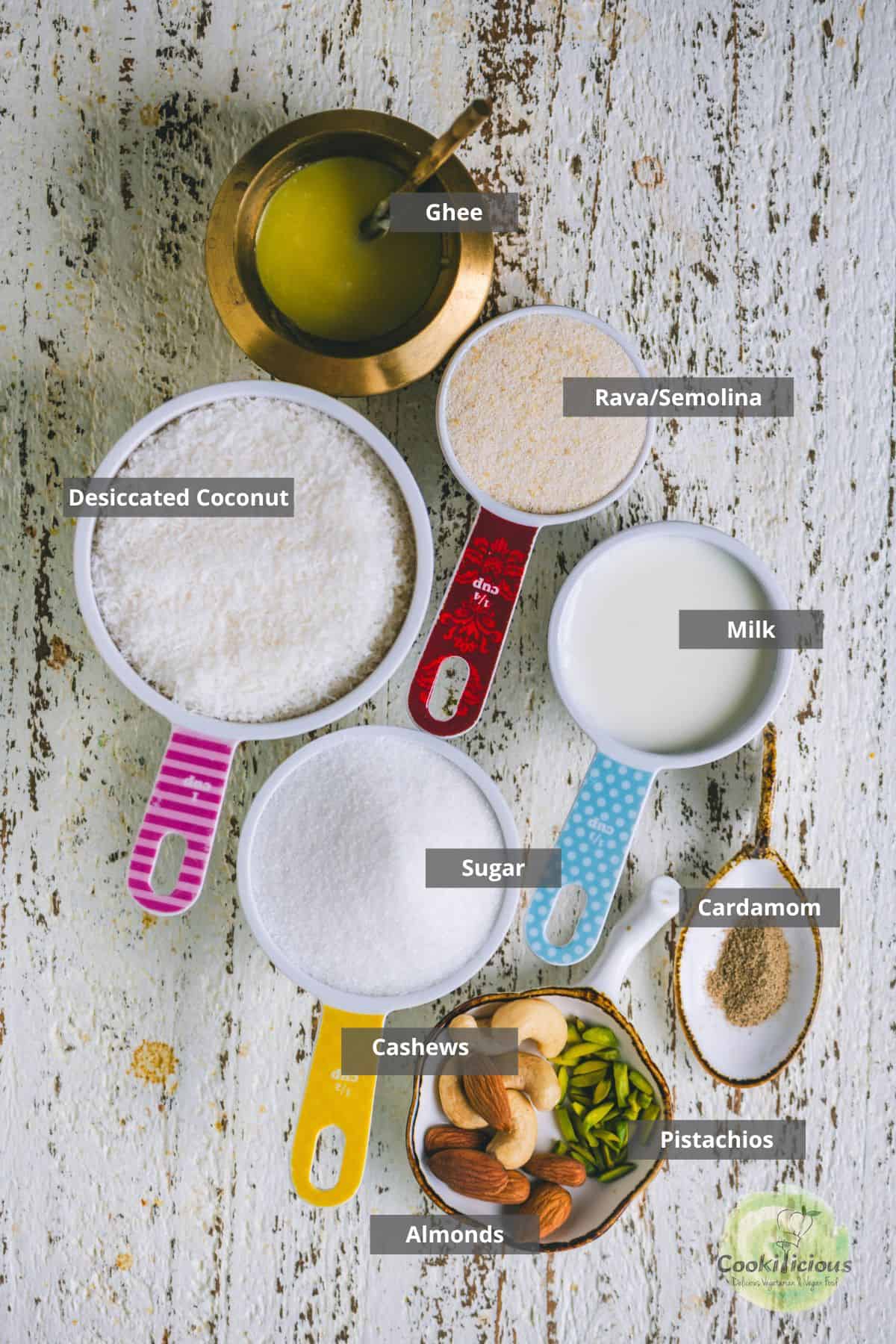 Ingredients for caramel coconut barfi — ghee, desiccated coconut, rava/semolina, milk, sugar, cashews, almonds, and pistachios laid out in labeled measuring cups.